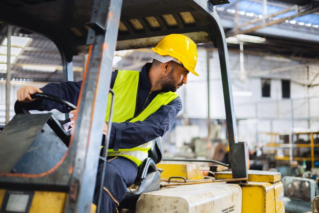 worker wearing helmet with driving forklift backwards in warehouse